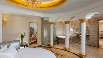 A luxurious hotel room with a large bed, a chandelier, a painting, a bathroom with a bathtub, and a marble floor.