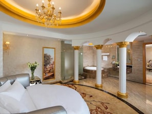 Ein luxuriöses Hotelzimmer mit einem großen Bett, einer Kristallleuchter, einem Gemälde, einem Badezimmer mit einer Badewanne und einem Marmorboden.
