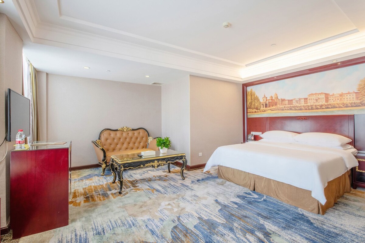 Ein Hotelzimmer mit Bett, einer Sitzecke, einem kleinen Tisch, einem Fernseher und einem Bild an der Wand.