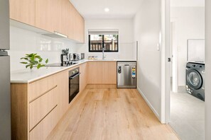 A modern kitchen with wooden cabinets, a stainless steel refrigerator, a dishwasher, and a washing machine. - Brand-New Home | Walk to Beach & Dining | full A/C (Surfers Paradise)