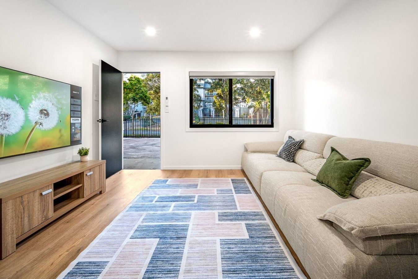 Uma sala de estar moderna com televisão de tela plana, um sofá, um tapete estampado e uma janela com vista para o exterior.