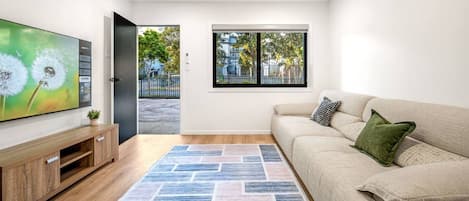 Uma sala de estar moderna com televisão de tela plana, um sofá, um tapete estampado e uma janela com vista para o exterior.