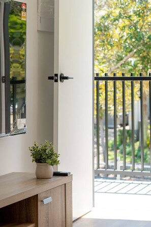A door with a black handle, a potted plant on a wooden console, and a view of a garden through a glass door. - New Stylish| Walk to Beach & Cavill Ave | full A/C (Surfers Paradise)