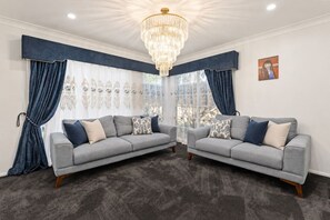 A room with two grey sofas, a chandelier, and a large window with curtains. - Family Retreat |Private Pool|Multi Living|Full AC (Forestdale)