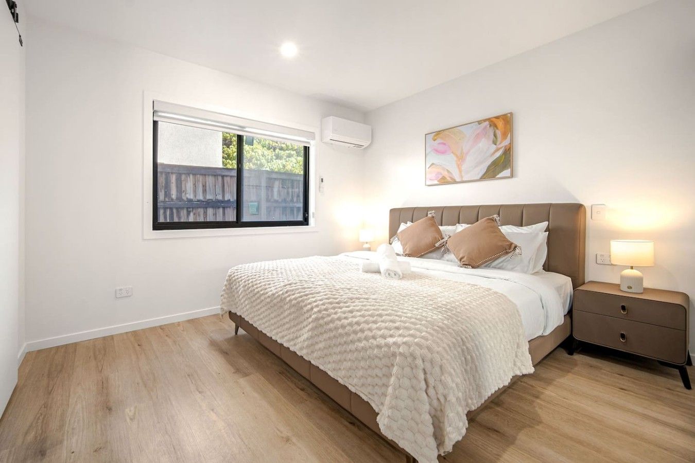 Une chambre à coucher avec un lit, des tables de chevet, une fenêtre et un tableau accroché au mur.