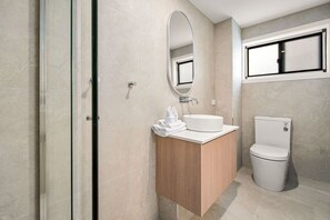 Ein modernes Badezimmer mit einer Duschkabine aus Glas, einem Holzbadezimmermöbel mit Waschbecken in Weiß und einer Toilette.