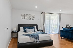A bedroom with a bed, bedside tables, a blue sofa, and a view through a window. - Prime Location| 3 Min to Westfield | Multi Living (Wishart)