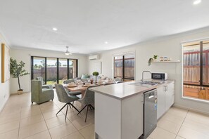 Une cuisine moderne dotée d’un îlot central, d’un coin repas avec des chaises et de grandes fenêtres.