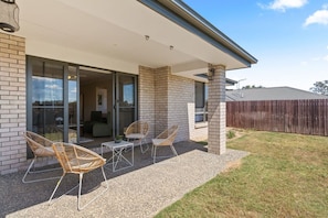 Ein modernes Haus mit überdachter Terrasse, Sitzgelegenheit im Freien und einer sichtbaren Garage.