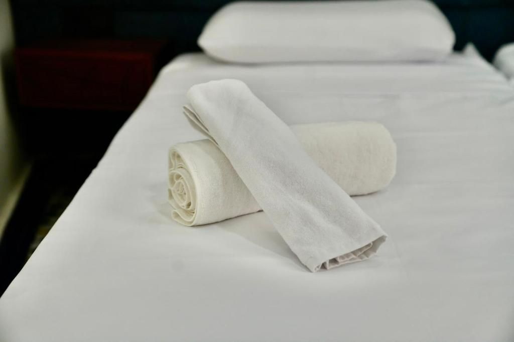 Una cama bien hecha con una toalla blanca y una toalla enrollada encima.