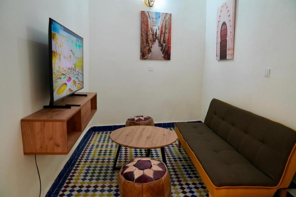 Una sala de estar con televisor, sofá, una mesa redonda de centro y otomanas.