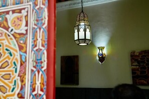 Un farol colgante con diseños intrincados, una pared con motivos geométricos y un pequeño cuadro enmarco.