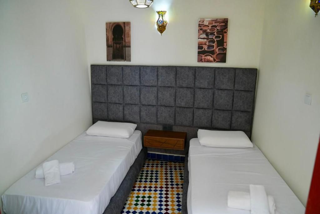 Una habitación con dos camas individuales, un cabecero acolchado gris, una mesita de noche de madera pequeña y un suelo con un estampado colorido.