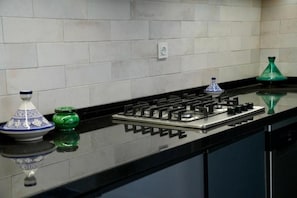 Cozinha com fogão a gás, bancada preta e objetos decorativos, incluindo uma tigela azul e branca e um vaso verde.