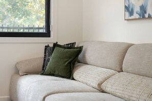 Un canapé beige agrémenté d’un coussin vert et d’un autre à motifs, le tout placé contre un mur avec une fenêtre.