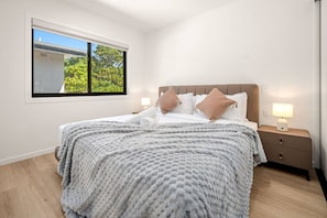 Une chambre à coucher avec un lit, des oreillers, une table de chevet, une lampe et une fenêtre donnant sur un paysage verdoyant.