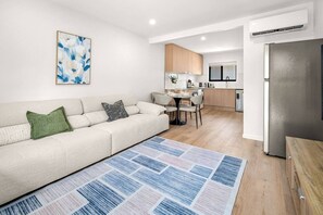 A modern living room with a sofa, a dining table, and a kitchen area in the background. - Brand-New|Walk to Cavill & Beach| Glink |Full A/C (Surfers Paradise)