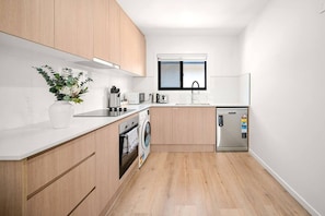 A compact kitchen with wooden cabinets, a built-in oven, a washing machine, and a refrigerator. - Brand-New|Walk to Cavill & Beach| Glink |Full A/C (Surfers Paradise)