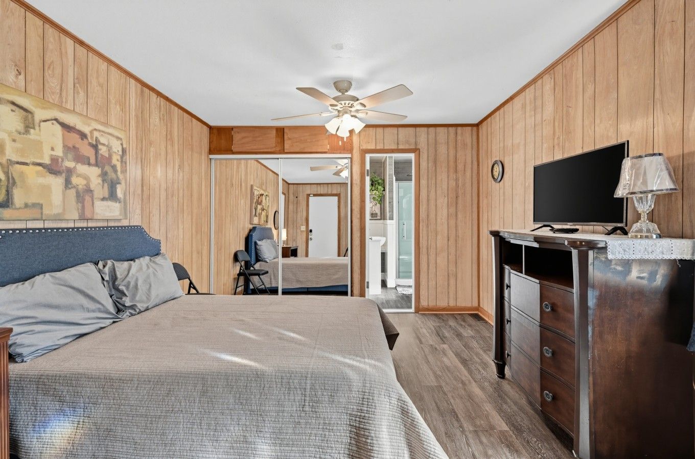 Een slaapkamer met een bed, een dressoir, een televisie en een plafondventilator.