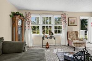 A living room with a sofa, a chair, a table with a vase, a clock, and a window with curtains. - Near MCAS New River - Peaceful Home w Patio (Jacksonville)