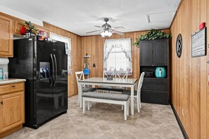 Une cuisine équipée d’un réfrigérateur, d’une table à manger avec des chaises et d’un ventilateur de plafond.