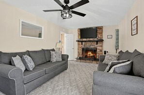 A living room with a fireplace, two grey sofas, a ceiling fan, and a TV mounted above the fireplace. - Near MCAS New River - Peaceful Home w Patio (Jacksonville)