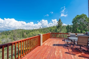A wooden deck with a red railing, outdoor furniture, and a view of a forested landscape. - Casa Oso Grande - Hot Tub, Deck, Fireplaces, Games (Ruidoso)