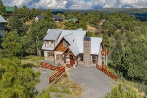 A two-story lodge with a stone facade, a metal roof, and a wooden deck. - Casa Oso Grande - Hot Tub, Deck, Fireplaces, Games (Ruidoso)