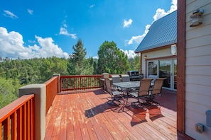 A deck with a table and chairs, overlooking a forested area. - Casa Oso Grande - Hot Tub, Deck, Fireplaces, Games (Ruidoso)