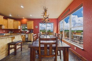 A spacious kitchen with wooden cabinets, a large dining table, and a view of the outdoors through a large window. - Casa Oso Grande - Hot Tub, Deck, Fireplaces, Games (Ruidoso)