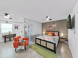 Um quarto moderno com cama, duas cadeiras, escrivaninha e televisão.