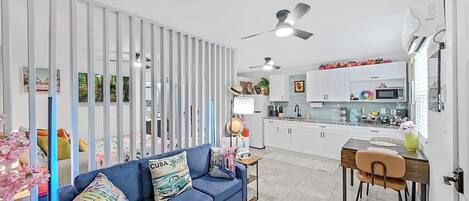 A modern living room with a blue sofa, a dining area with a wooden table and chairs, and a kitchen with white cabinets and a microwave.