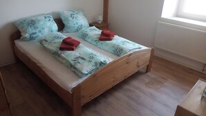 Uma cama de solteiro com estrutura de madeira, duas almofadas com padrão floral e duas toalhas vermelhas.