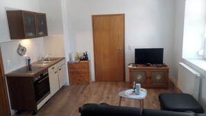 Un ambiente compatto con angolo cottura, televisione e divano.