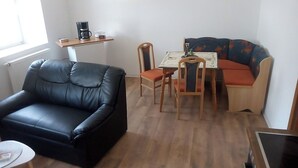 Uma sala de estar com um sofá de couro preto, uma mesa de jantar de madeira com cadeiras e um sofá colorido.