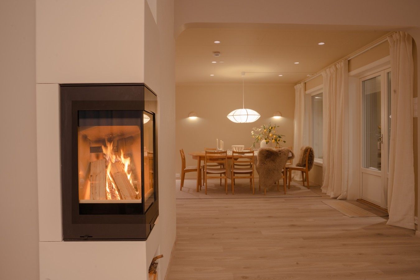 A modern interior with a fireplace, dining area, and a large window with curtains.