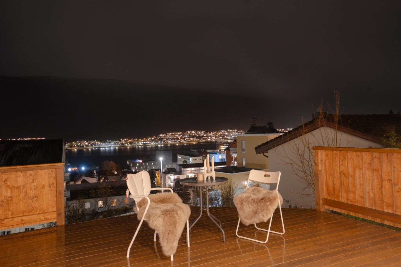 Une terrasse avec deux chaises et une table, offrant une vue sur le paysage urbain illuminé la nuit.