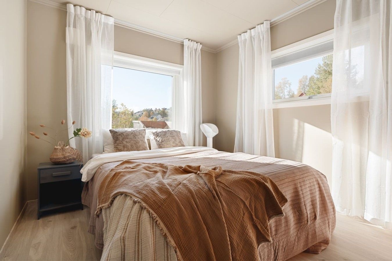 Une chambre à coucher avec un lit, une table de chevet, une lampe et une fenêtre avec des rideaux.
