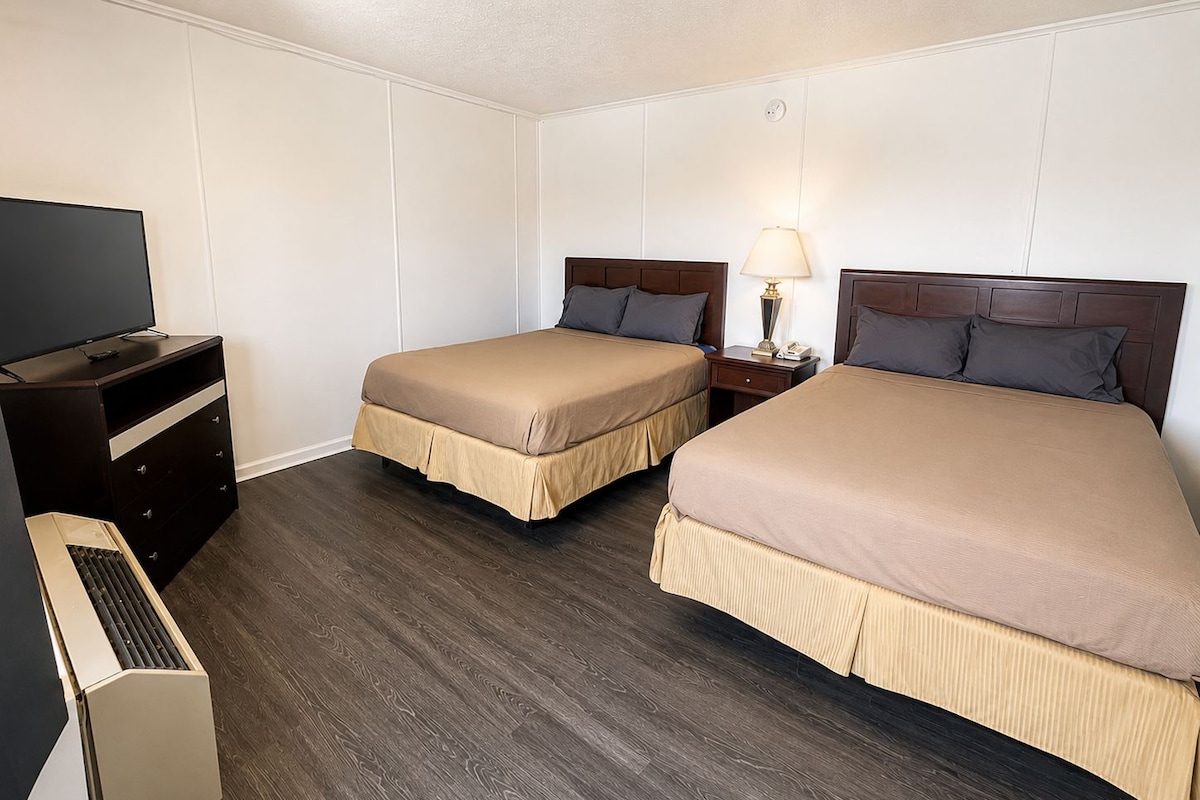 Habitación de hotel con dos camas, televisión, escritorio y lámpara.
