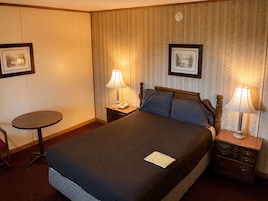 Habitación de hotel con cama, dos mesitas de noche con lámparas, una pequeña mesa redonda y dos cuadros en la pared.