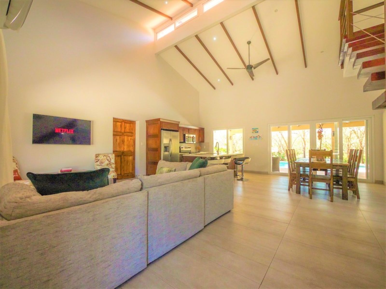 A spacious living area with a large sofa, a TV mounted on the wall, and a ceiling fan.