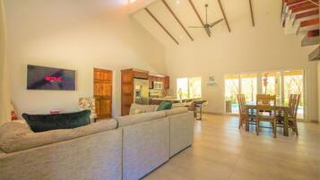 A spacious living area with a large sofa, a TV mounted on the wall, and a ceiling fan.