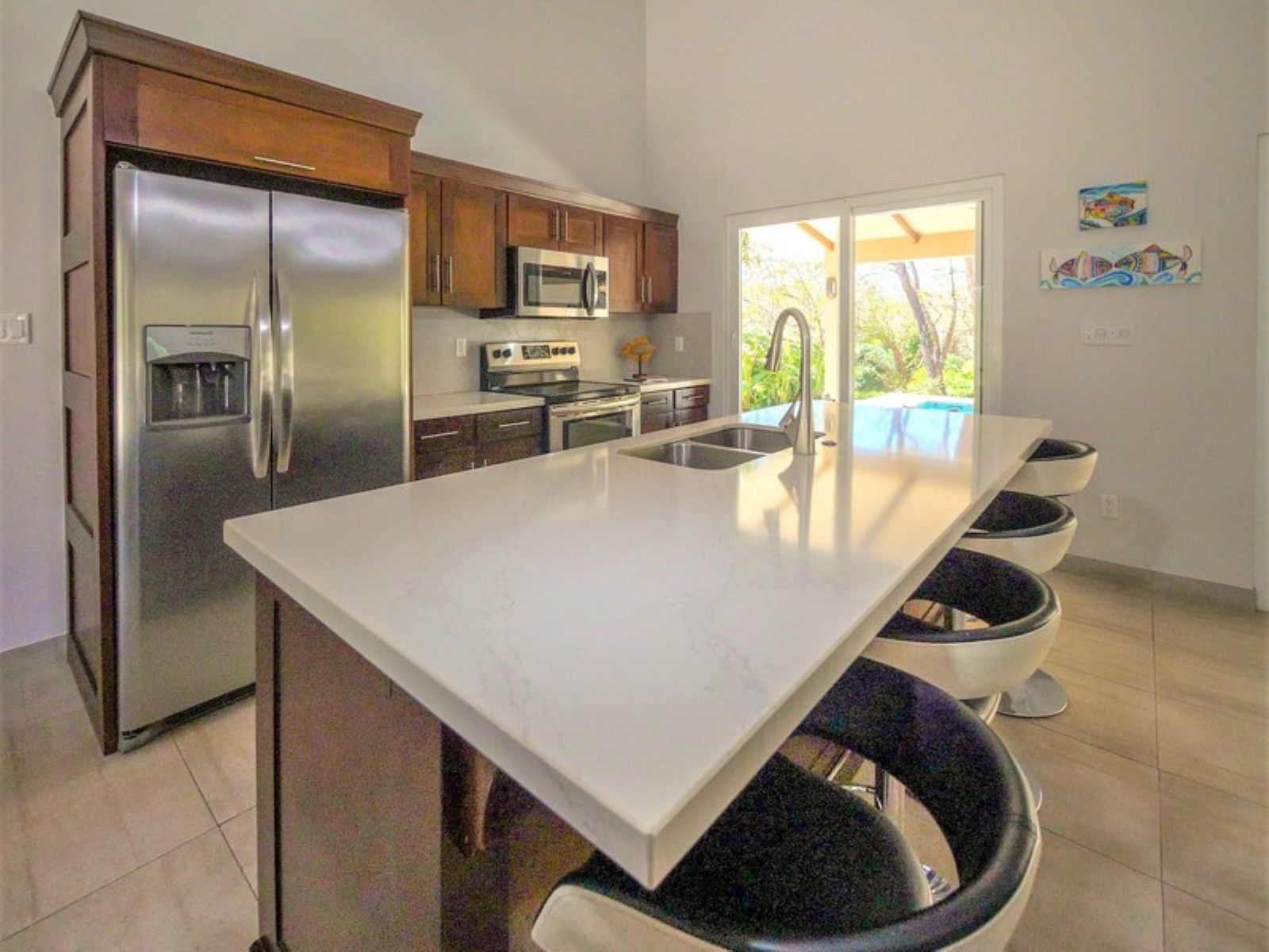 A modern kitchen with a large island, stainless steel appliances, and a view to an outdoor area.