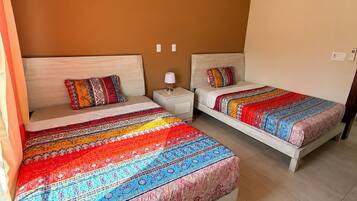Quarto com duas camas, cada uma com roupa de cama estampada, mesa de cabeceira com abajur e um aparelho de ar condicionado na parede.
