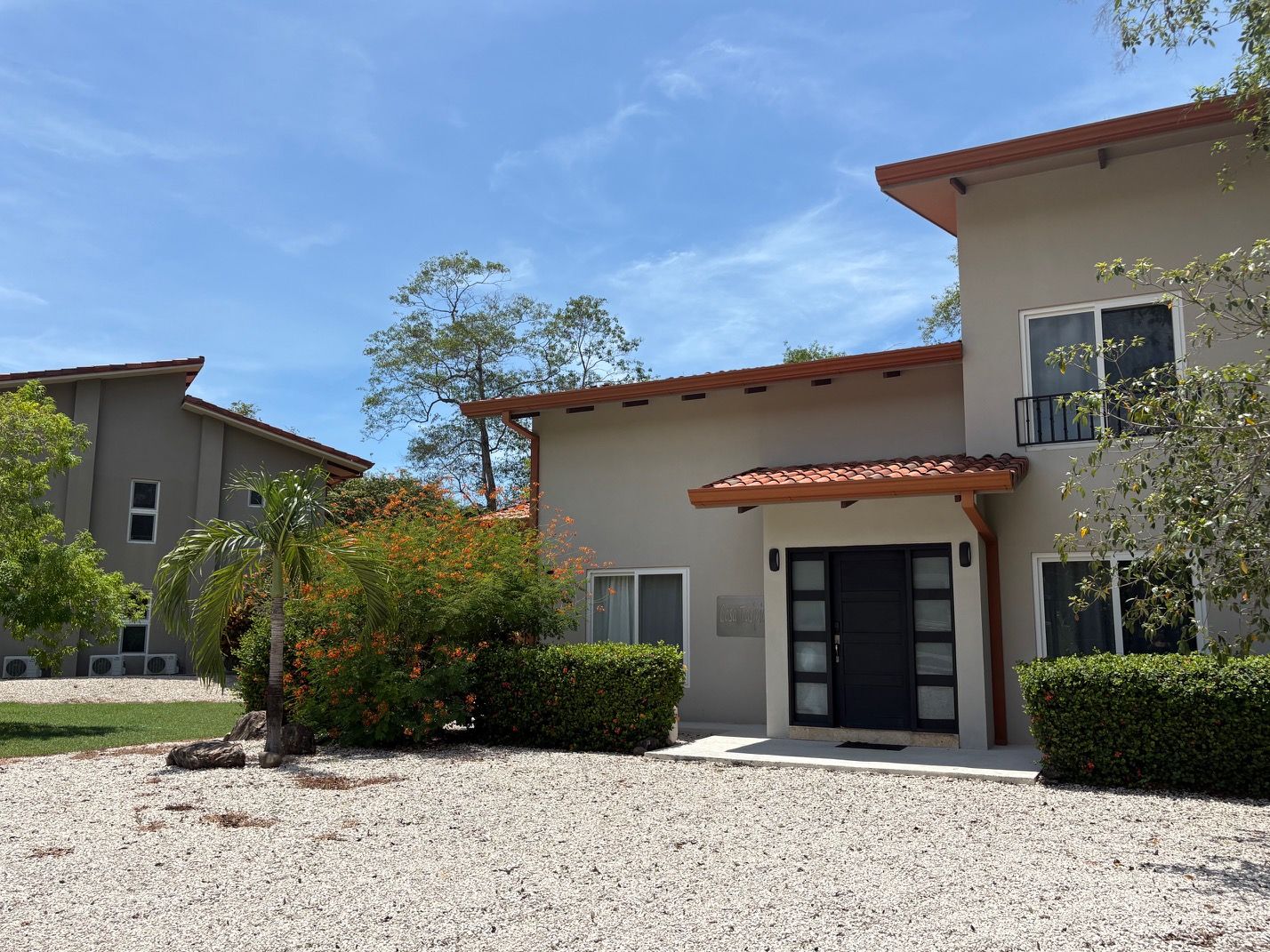 A two-story building with a gravel driveway, a black door, and a small balcony.