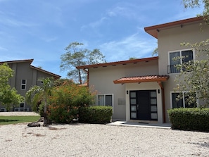 A two-story building with a gravel driveway, a black door, and a small balcony. - Tropical Villa • Private Pool • Near Conchal & Flamingo (Brasilito)