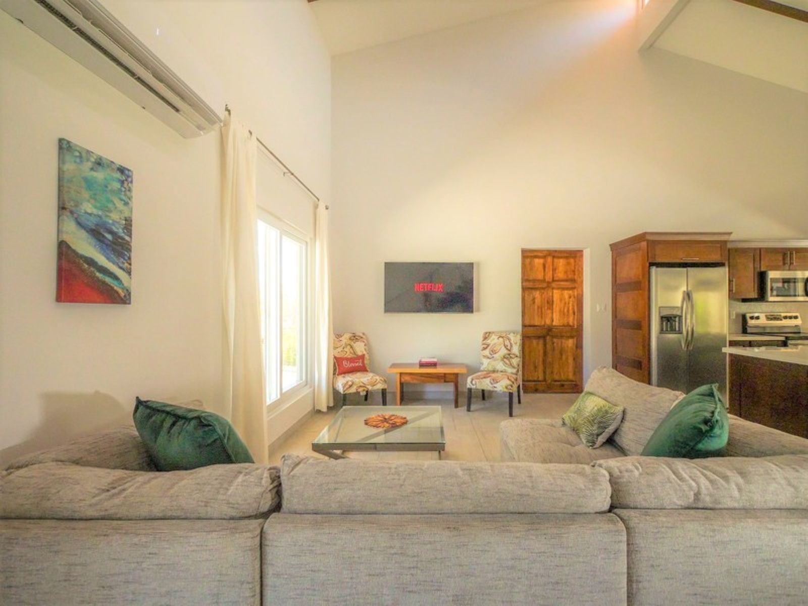 A living room with a sofa, two chairs, a coffee table, and a kitchen area with a refrigerator and microwave.