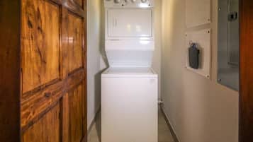 A compact laundry room with a front-loading washer and dryer, wooden cabinets, and a utility panel on the wall.