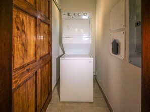 Una bugaderia reduïda amb rentadora i assecadora de càrrega frontal, armaris de fusta i un quadre elèctric a la paret.