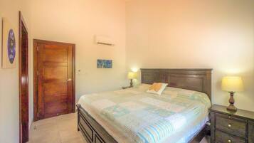 A bedroom with a bed, two bedside tables, a ceiling fan, a door, and a wall-mounted air conditioning unit.